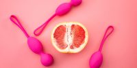 Metaphor for pelvic floor exercises, gynecology and treat urinary incontinence through strength exercise concept with kegel weights and half a grapefruit isolated on pink background